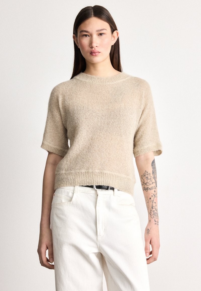 Trumpomis rankovėmis megztinis smėlio spalvos, su ribbiniu apačios ir rankogalių raštu, derinamas su baltais džinsais. Minkšta tekstūra, laisvo stiliaus prigludimas.