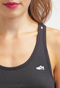 Black tank top made of cotton, featuring a low neckline and a small Nike logo on the left side. Smooth texture, lightweight design.
