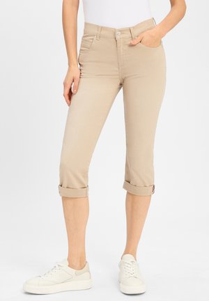 Beige, cropped Jeans aus Baumwollmischung mit aufgerollten Säumen und Vordertaschen; getragen mit weißen Sneakers.