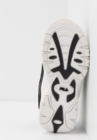 Sorte og hvite sneakersåler har et teksturert gummidesign med spor og utskjæringer, merket med et "Fila"-logo i midten.
