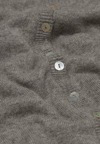 Grauer Strickcardigan mit geripptem Kragen, ausgestattet mit mehreren hellen, runden Knöpfen aus Muschel. Weicher Stoff mit einer sanft zerknitterten Textur.
