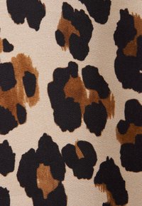 Gros plan d'un tissu avec des taches irrégulières noires et marron à motif léopard sur un fond beige.