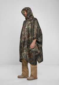 Maastoväri poncho, joka on valmistettu vedenpitävästä kankaasta, hupullinen ja jossa on vihreän, ruskean ja mustan värin yhdistelmiä; löysä istuvuus.