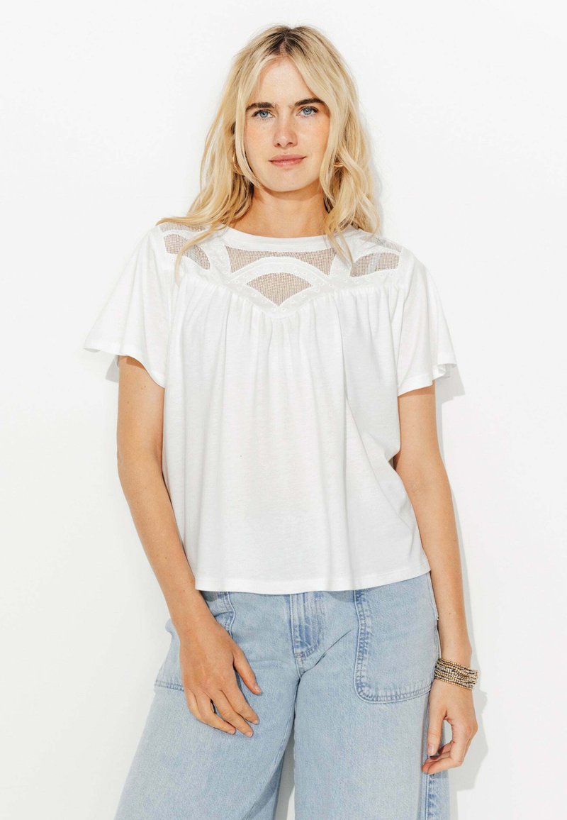 Haut blanc à manches courtes avec un empiècement en maille semi-transparente au design géométrique. Coupe décontractée, tissu doux et détails froncés au niveau de la poitrine.