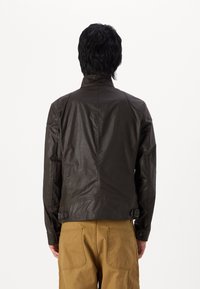 Καφέ δερμάτινο μπουφάν με ψηλό γιακά, κομψό σχέδιο και διακριτές ραφές, συνδυασμένο με χακί παντελόνι.