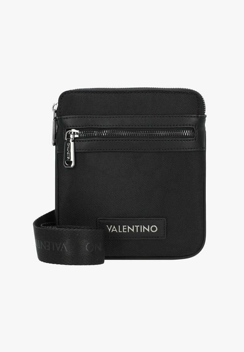 Sac à bandoulière noir en nylon texturé avec un compartiment zippé, arborant un patch en cuir avec logo et une sangle en tissu ajustable.