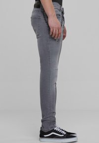 Szare dżinsy slim-fit z przetarciami, z łańcuchem przymocowanym do pasa, w połączeniu z czarnymi sneakersami i białymi akcentami.