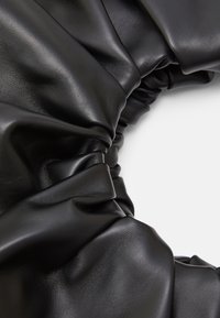 Zwarte leren haarband met een gerimpeld ontwerp, dat een gladde textuur en zachte glans laat zien, ideaal om het haar veilig vast te houden.