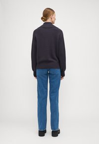 Marineblå strikkegenser med høy krage, ribbestrikkede ermer og linning. Kombinert med lyseblå rette jeans og svarte plattform sko.