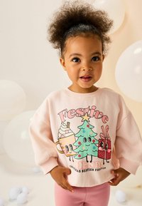 Helles rosa Sweatshirt mit einer bunten Grafik von einem Baum, Geschenken und einem Getränk, getragen über passenden rosa Leggings. Weiche Textur.