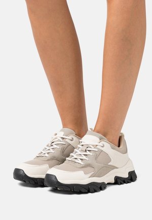 Sneakers in mesh beige e bianco con pannelli testurizzati, suola in gomma robusta e suola esterna nera a contrasto. I lacci sono bianchi; include colletto imbottito.