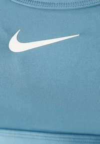 Svijetloplava Nike sportska brassiere od glatkog materijala, s bijelim logom, rebrastom teksturom i urednim šavovima duž rubova.