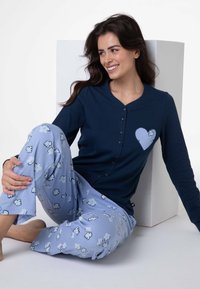 Maglia a maniche lunghe blu navy con bottoni e un disegno a forma di cuore sul petto, abbinata a pantaloni del pigiama azzurri chiaro con motivo floreale.