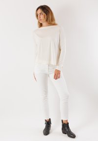 Top a maniche lunghe color crema realizzato in tessuto morbido, abbinato a jeans skinny bianchi e stivali neri alla caviglia con dettagli in cerniera.