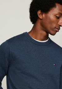 Maglione a maglia blu navy con scollo rotondo, dotato di un piccolo logo sul petto e polsini e orlo a costine. Texture liscia.