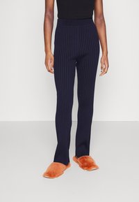 Mörkblå ribbade byxor med en åtsittande midjeband, gjorda av mjukt material, kombinerat med orange fluffiga tofflor. Byxorna har en rak bendesign.