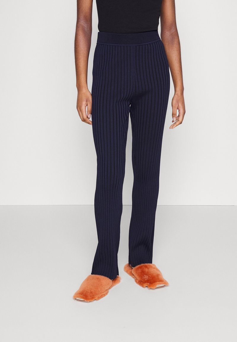 Mörkblå ribbade byxor med en åtsittande midjeband, gjorda av mjukt material, kombinerat med orange fluffiga tofflor. Byxorna har en rak bendesign.