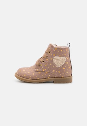 Botte marron pour enfant à lacets avec motifs de cœurs jaunes et un patch cœur texturé beige sur le côté, semelle couleur sable et languette à l'arrière.