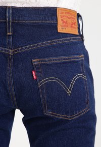 Jeans in denim blu scuro con un patch posteriore con branding, cuciture in contrasto e un design distintivo delle tasche curve.