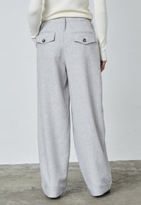 Lys grå vidde bukser i et struktureret stof, med to bagside lommer med knaplukninger og et høj talje design.