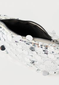 Ασημένια τσάντα χειρός με παγιέτες και φερμουάρ, με δομημένο σχήμα, μαύρη εσωτερική επένδυση και αντανακλαστικές κυκλικές παγιέτες στην επιφάνεια.