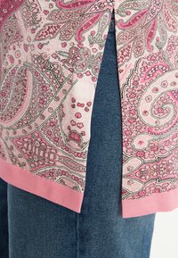 Lichtroze blouse met een paisleypatroon met accenten in donkerder roze, en een zoom met een effen roze rand, gecombineerd met denimstof.