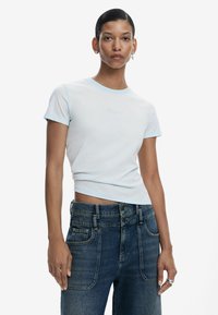 T-shirt cropped bleu clair avec un col contrastant bleu clair, associé à un jean en denim taille haute avec plusieurs boutons et poches.