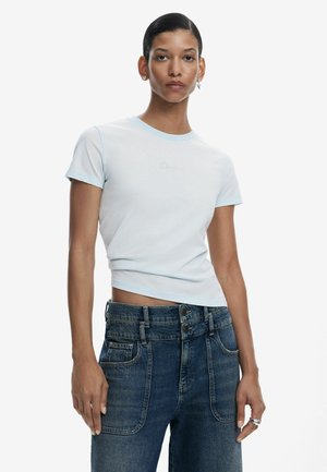 T-shirt cropped blu chiaro con collo a contrasto blu chiaro, abbinata a jeans di denim a vita alta con più bottoni e tasche.
