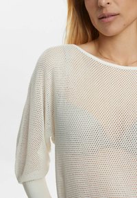 Weißer, luftiger Strickpullover aus Mesh mit lockerer Passform, weitem Ausschnitt und Dolmanärmeln. Verfügt über ein strukturiertes Muster und gerippte Bündchen.