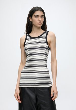 Young woman with long dark hair wears sleeveless black and white striped top and black pants against plain light background.
