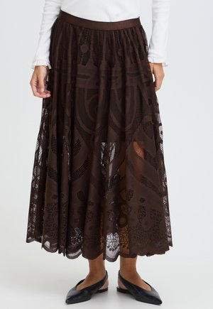 Jupe midi en dentelle marron à motifs abstraits portée avec un haut blanc à manches longues et des chaussures plates noires à bout pointu.