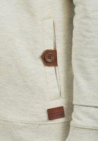 Lichtgrijze sweatshirt met een bruin leren patch en knop bij de zak, geribbelde manchetten en een zachte textuur.