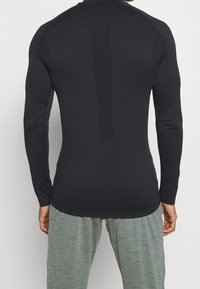 Person wearing a fitted long-sleeve black top and loose gray pants, viewed from the back against a plain background.