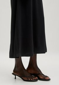 Zwart midi-jurk van zachte stof met een relaxte pasvorm, gecombineerd met zwarte sandalen met bandjes en een dunne zool en een kleine hak.