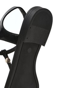 Sandalo nero con una fibbia in pelle testurizzata, punta tonda e suola in gomma rigata con una sezione liscia per il comfort.