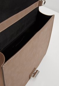 Torebka z tan faux leather o gładkiej teksturze, z klapką z przodu, zapięciem ze srebrnym okuciem oraz czarnym wnętrzem z kieszonką na suwak.