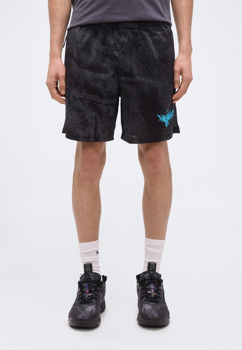 Άνδρας που φοράει μαύρο αθλητικό σορτς με υφή και μπλε λογότυπο φοίνικα, μαύρα αθλητικά παπούτσια και λευκές κάλτσες, στέκεται μπροστά σε απλό φόντο.