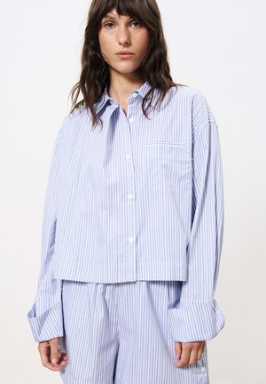 Hellblau gestreiftes Button-Down-Hemd mit einem cropped Design, breiten Manschetten und einer Brusttasche. Hergestellt aus einem weichen, leichten Stoff.