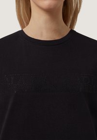 Černé bavlněné tričko s kulatým výstřihem a tónovaným logem z broušených kamínků přes hruď. Hladká textura, krátké rukávy.