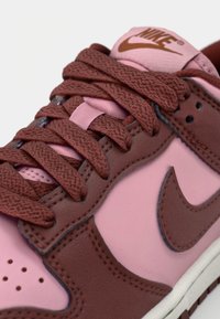 Sapatilhas Nike com um upper em pele rosa e detalhes em castanho, atacadores texturizados castanhos e um logo na língua; design de cano baixo.