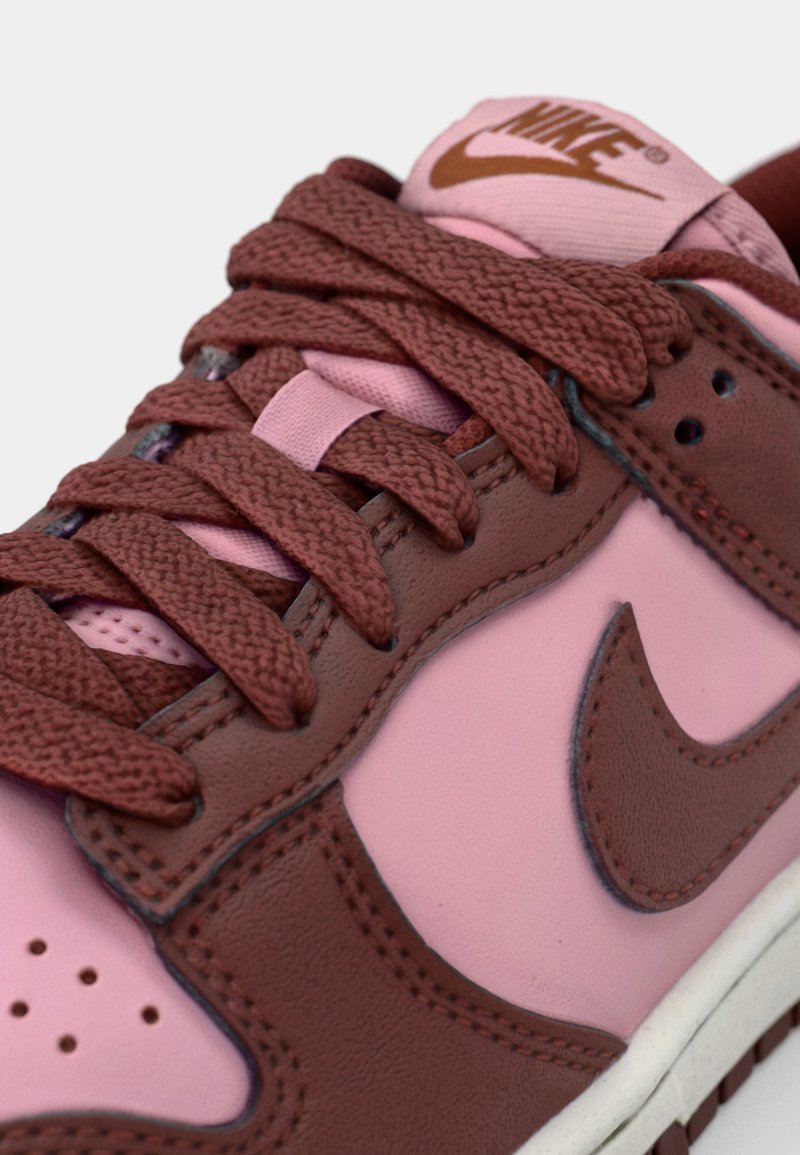 Sneakers Nike con una toma in pelle rosa e dettagli marroni, lacci marroni texturizzati e un logo sulla linguetta; design low-top.