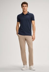 Marineblauw katoenen polo shirt met korte mouwen, een drieknopen placket en subtiele logodetails, gecombineerd met beige lichte broek en witte sneakers.