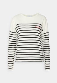 Långärmad skjorta, krämfärgad med svarta horisontella ränder, har en ficka med röd "måste ha" broderi, mjukt bomullsmaterial, avslappnad passform.