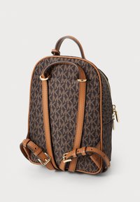 Zaino monogram marrone con spallacci e dettagli in pelle beige, chiusura a cerniera e hardware in tonalità dorata, caratterizzato da un design strutturato e curvo.