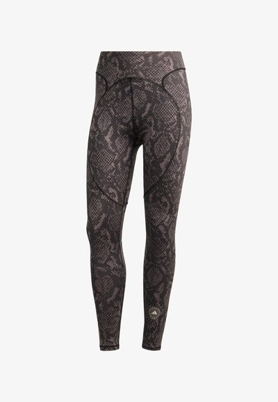 Legíny s černým a šedým hadím vzorem, vysokým pasem a logem Adidas od Stelly McCartney poblíž levého kotníku.