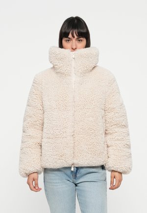 Beige nepbontjas met een hoge kraag, rits aan de voorkant en elastische zoom. Het materiaal is gestructureerd en pluizig, wat warmte biedt.