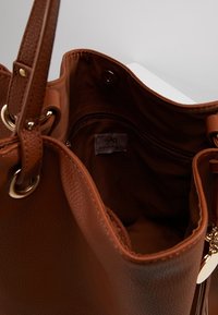 Brun læderhåndtaske med tekstureret yderside, guldfarvet hardware og et rummeligt indre med en lynlåslomme og mærkelogo.