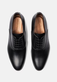 Zwarte leren nette schoenen met een gladde afwerking, spitse neus en een vetersluiting met zes oogjes. Het interieur heeft een bronzen accent op de binnenzool.