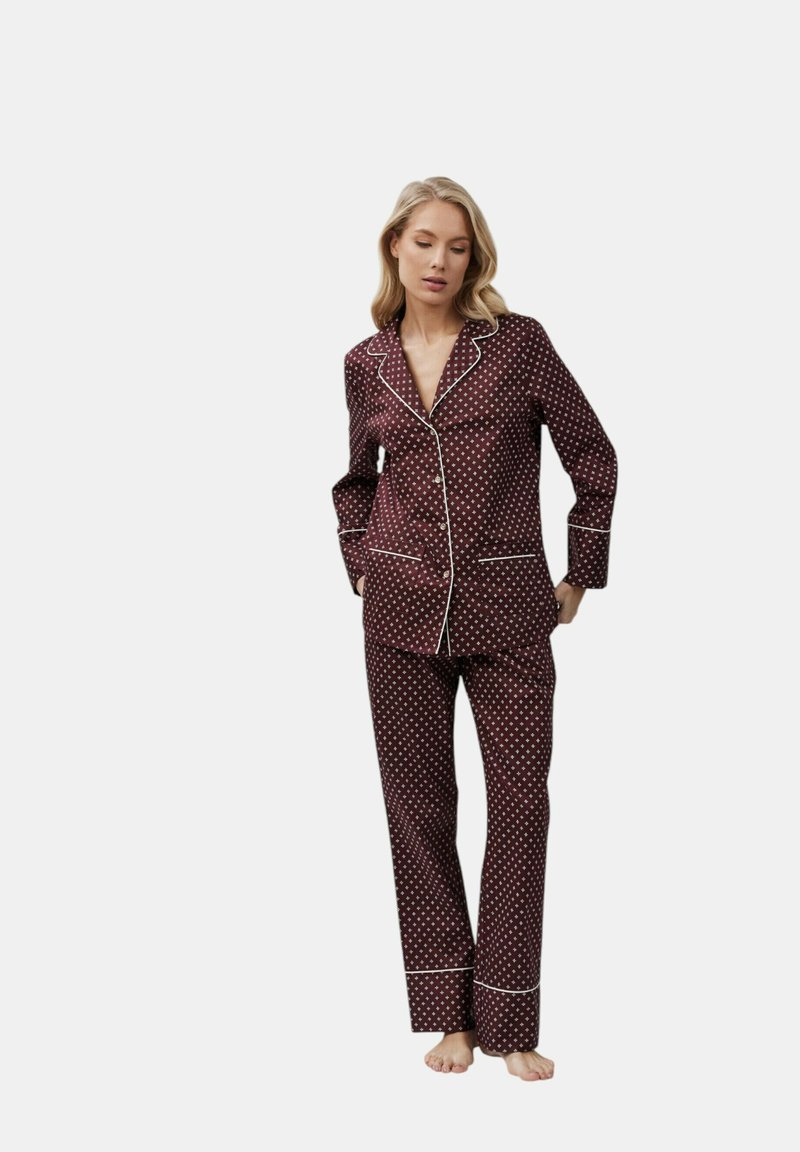 Set di pigiama bordeaux in satin con pois bianchi, dotato di colletto a punte, chiusura frontale con bottoni e piping bianco su polsini e pantaloni.