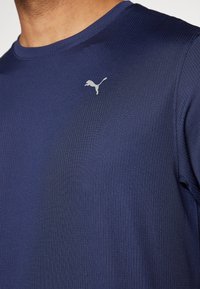 Temno modra športna majica z rebrasto strukturo, okrogel ovratnik, z majhnim srebrnim logotipom Puma na levem prsnem predelu.